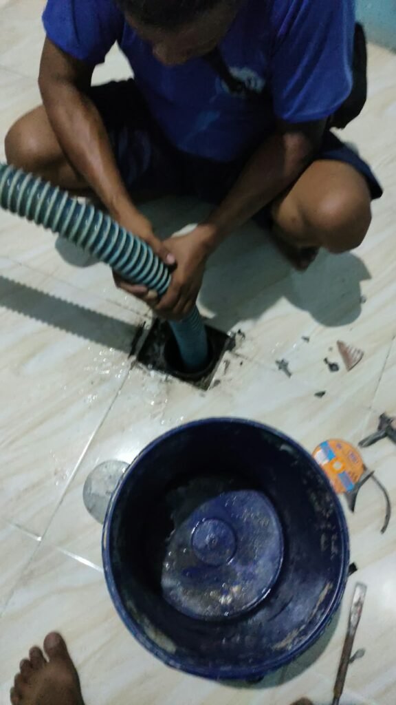 Petugas Raja Limbah menyedot lubang saluran di lantai kamar mandi dengan selang mesin vakum